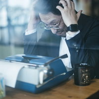 タイプライターの前で頭を抱えて考える男性の写真
