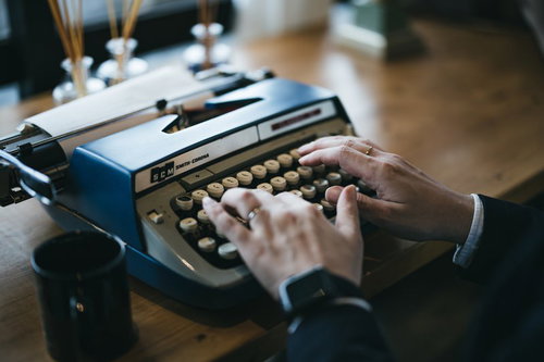 青いタイプライターを打鍵する手元