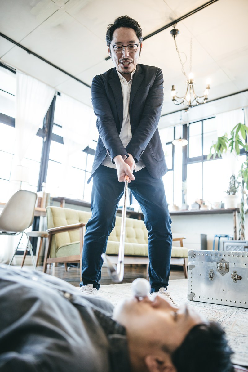 スーツ姿の男性がゴルフクラブのアイアンを両手で持ち威嚇するポーズ［モデル：ゆうせい 大川竜弥］
