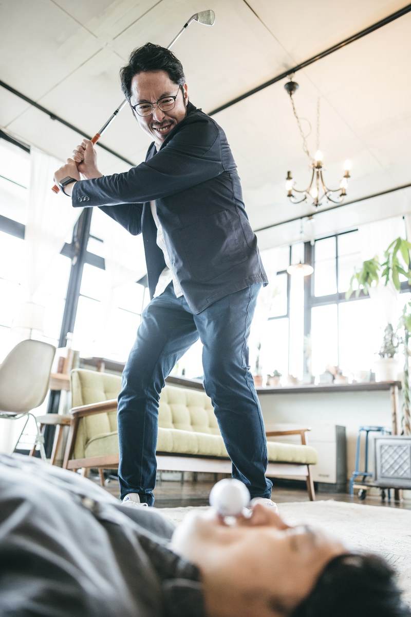 室内でゴルフクラブのアイアンを振り上げて威嚇するような姿勢の男性［モデル：大川竜弥 ゆうせい］