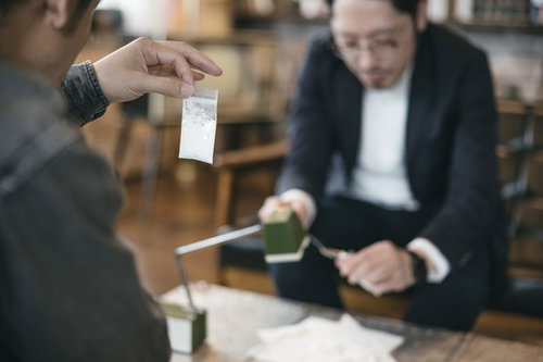 パケに入った白い粉（片栗粉）を相棒に見せる男性