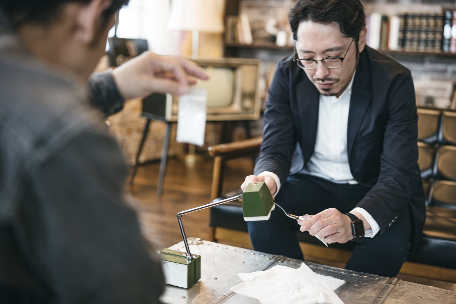 机の上で白い粉をパケに詰めているスーツ姿の男性［モデル：ゆうせい 大川竜弥］
