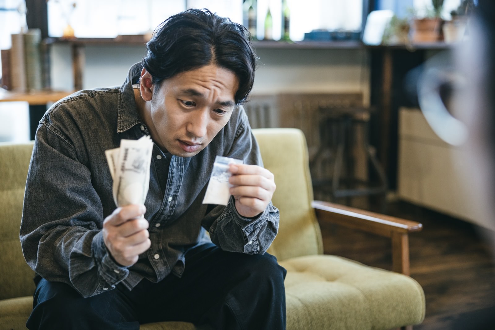 パケに入った白い粉を手に持ち真剣な表情で見つめるスーツ姿の男性［モデル：大川竜弥］