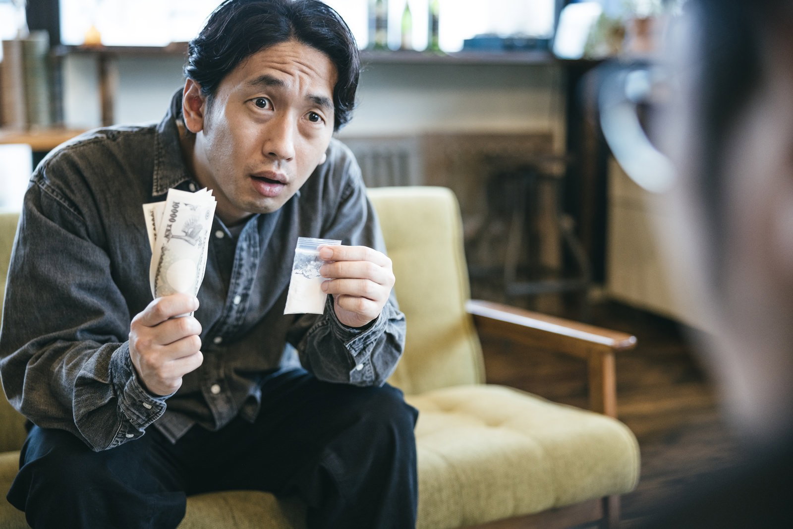 スーツを着た男性が白い粉の入った袋を手に持ち取引を持ち掛けている様子［モデル：大川竜弥］