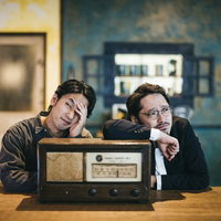 ラジオを前に頭を抱えて落ち込む二人組の探偵の写真