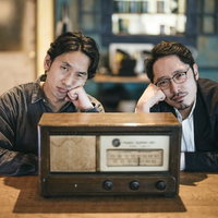アンティークラジオを挟んで頬杖をつく二人組の探偵の写真