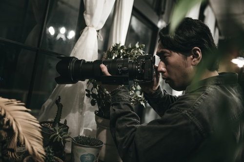 窓越しから望遠レンズでスクープを狙う男性カメラマン