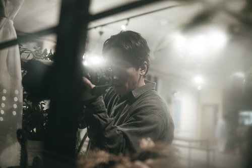 暗い場所から望遠レンズを構えて隠れてスクープを狙うパパラッチ男性