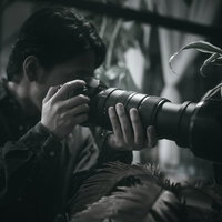 暗い場所で望遠レンズを構えて隠れて激写するカメラマンの写真