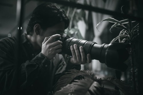 暗い場所で望遠レンズを構えて隠れて激写するカメラマン