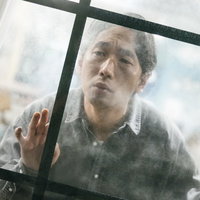 窓ガラスから張り込みする探偵の男性調査員の写真