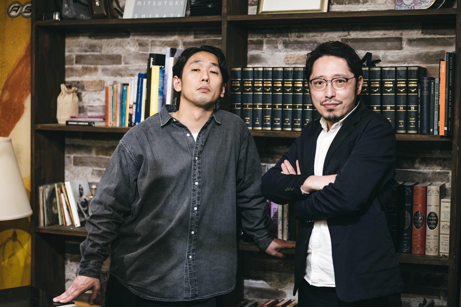 腕組みをして立つ二人の男性、背景に本棚がある室内［モデル：大川竜弥 ゆうせい］