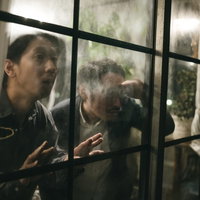 窓越しに張り込みをする探偵の男性ふたり、監視中の写真