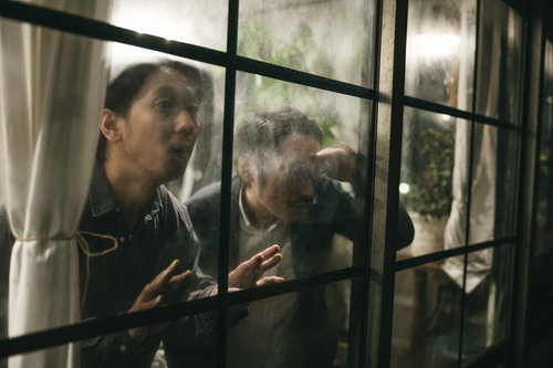 窓越しに張り込みをする探偵の男性ふたり、監視中