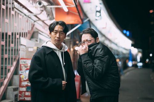 都橋商店街の夜間に立つ探偵姿の男性2人が会話する下町風景