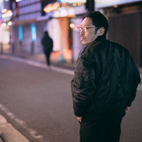 夜の街を歩く追跡者の後ろ姿、眼鏡の男性が黒いジャケット姿で尾行調査の写真