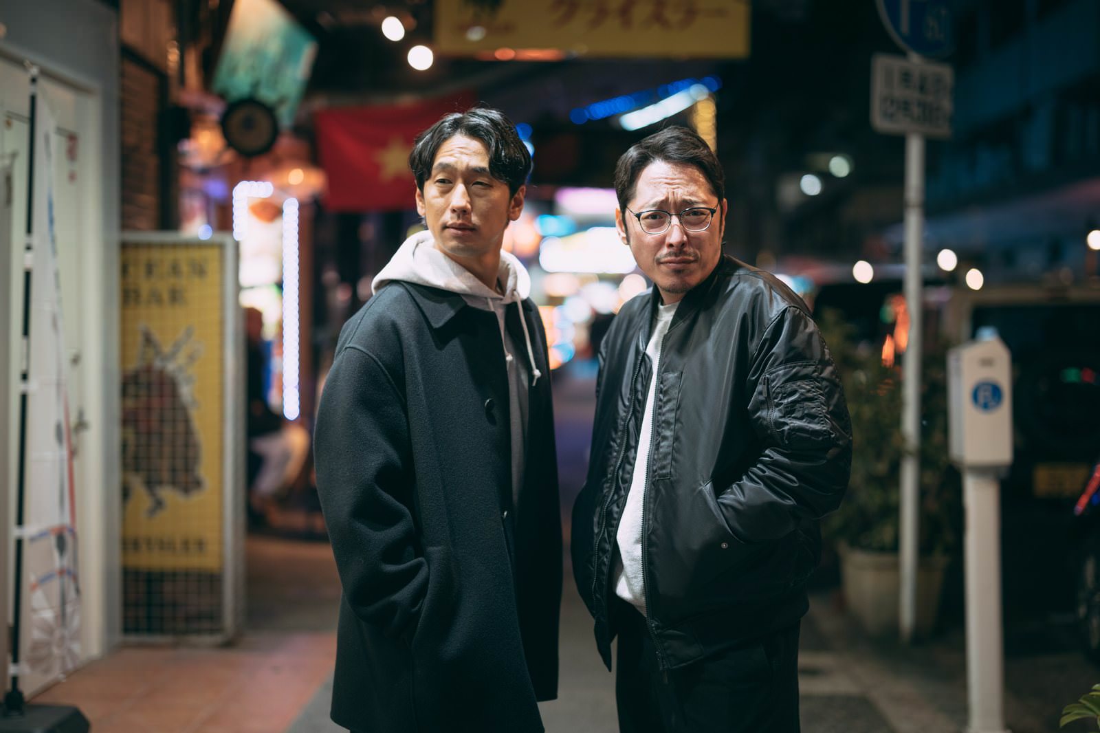 夜の下町商店街を探索する黒い上着を着た二人の男性［モデル：ゆうせい 大川竜弥］