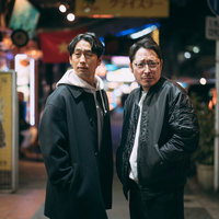 夜の下町商店街を探索する二人の男性、ネオン看板が光る繁華街の写真