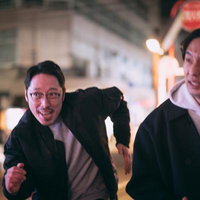 夜の繁華街を走り抜ける探偵と調査員の二人組の写真