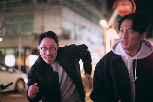 夜の繁華街を走り抜ける探偵と調査員の二人組