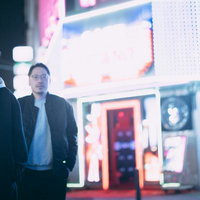 ネオンが輝く繁華街の店先で事情聴取する二人組の男性の写真