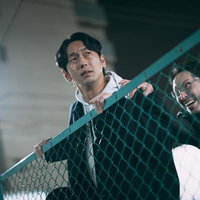 緑色フェンス越しに全力で逃走する二人の男性の写真