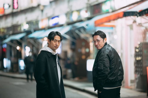 夜の街をうろつく二人の男性が駅前で周囲を警戒しながら会話