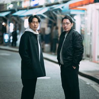 夜間の繁華街で立ち止まる探偵ストリートスナップの写真