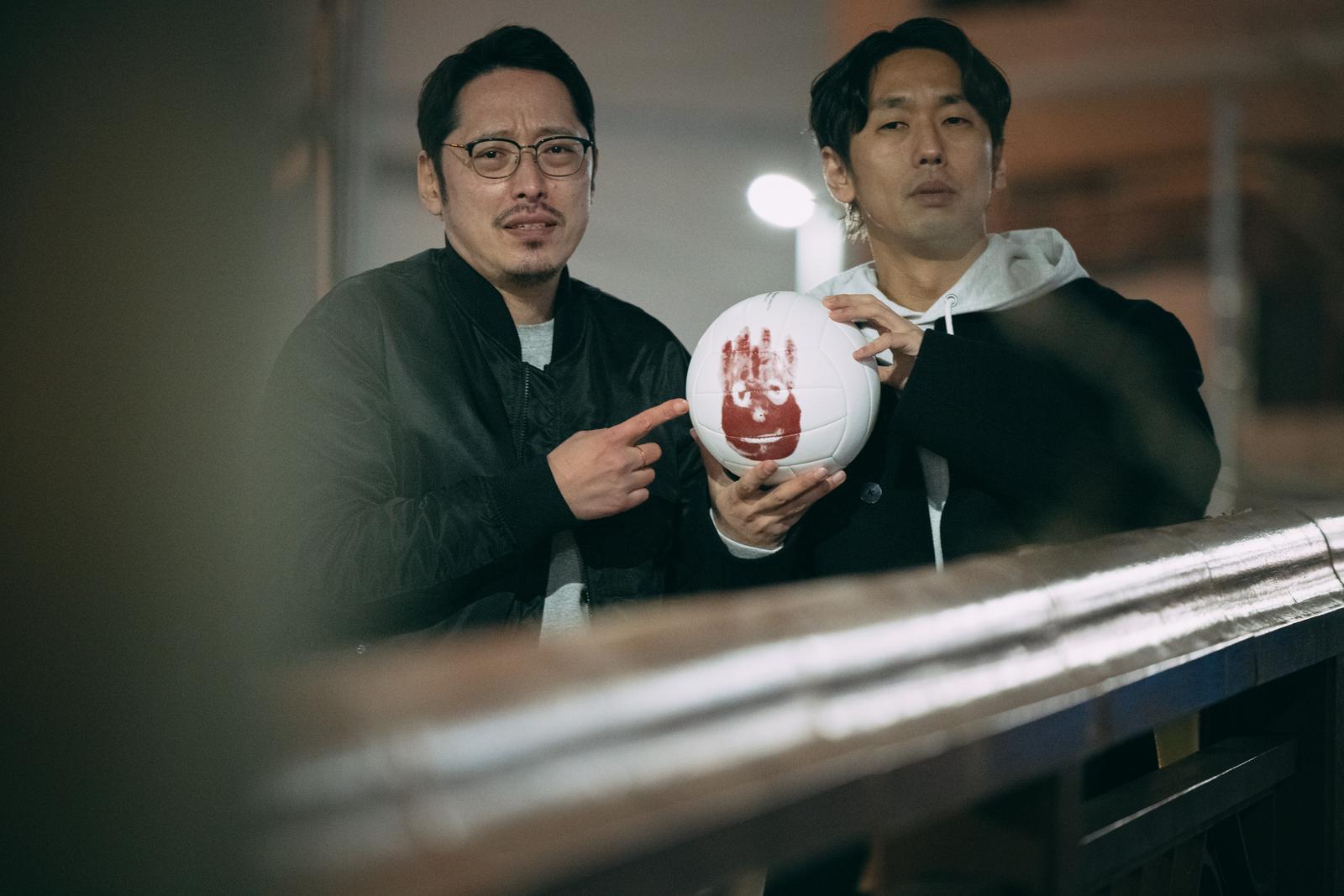 白と赤のボールを持つ眼鏡をかけた男性と黒いフーディーを着た男性の二人［モデル：大川竜弥 ゆうせい］