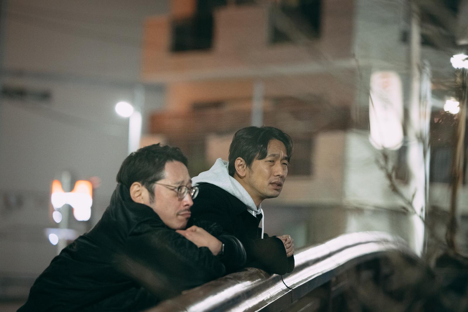 夜間の街で尾行・見張りについて語る二人組の男性探偵［モデル：大川竜弥 ゆうせい］