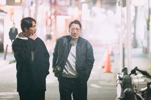 夜の繁華街を歩く二人の男性、尾行調査のシーン