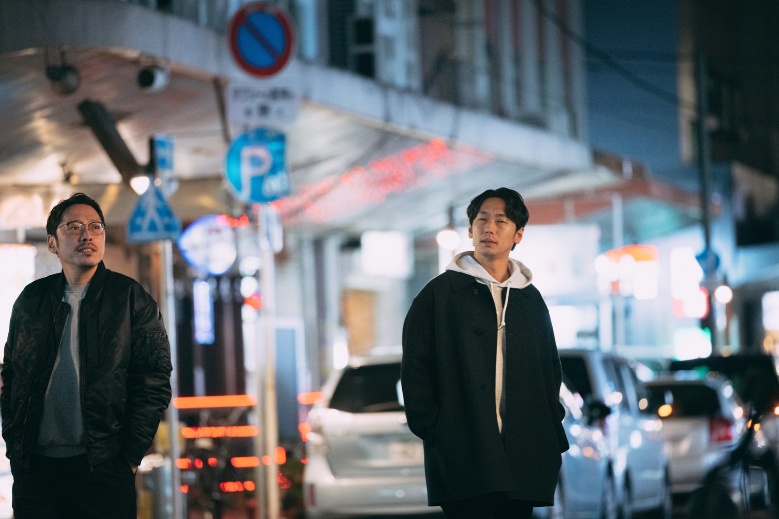 夜間の商店街で調査する二人の男性探偵が異なる方向に向かって歩いている［モデル：大川竜弥 ゆうせい］