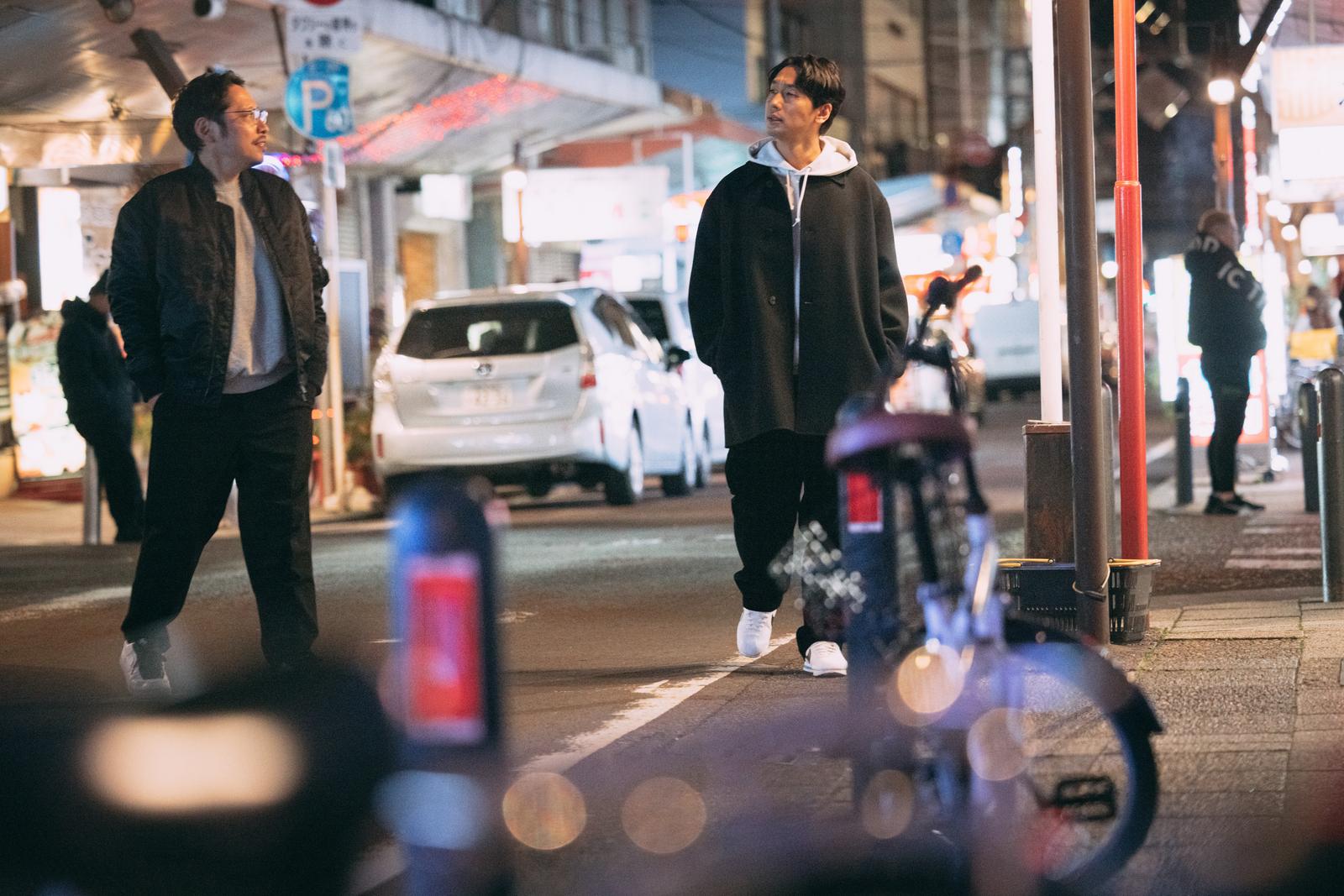 Two men walking on a sidewalk lit by street lights at night