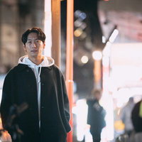 夜の繁華街で周辺を警戒する探偵の男性、ネオン街での調査風景の写真