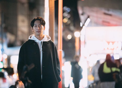 夜の繁華街で周辺を警戒する探偵の男性、ネオン街での調査風景