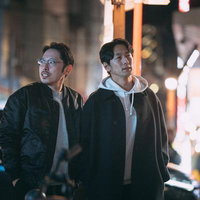 夜の繁華街をネオンの光の中で歩く二人の男性の写真