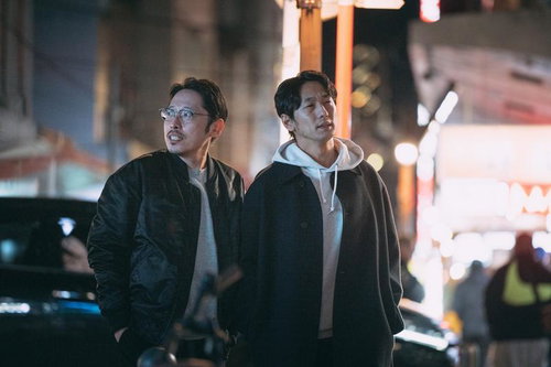 夜の繁華街をネオンの光の中で歩く二人の男性