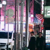 夜の繁華街でネオンに照らされながら歩く男性二人組の写真