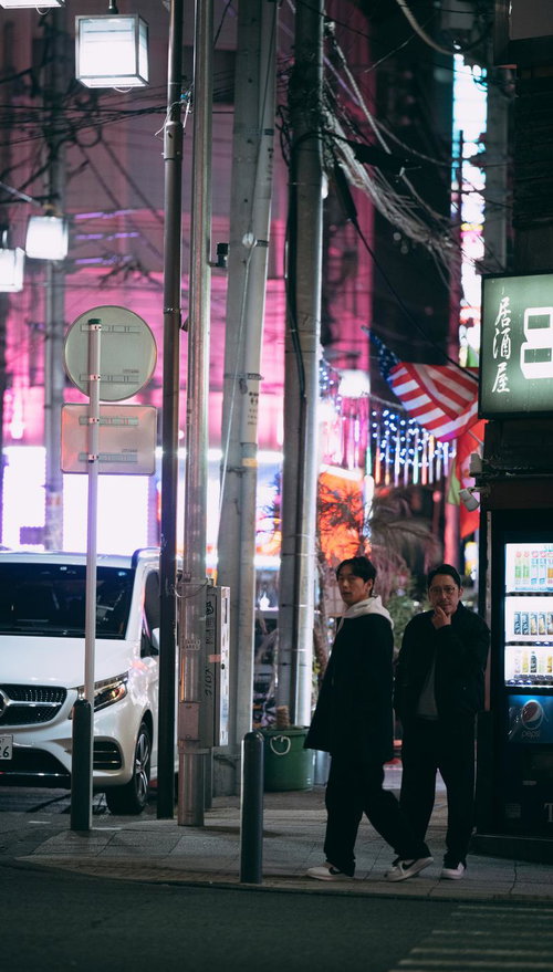 夜の繁華街でネオンに照らされながら歩く男性二人組