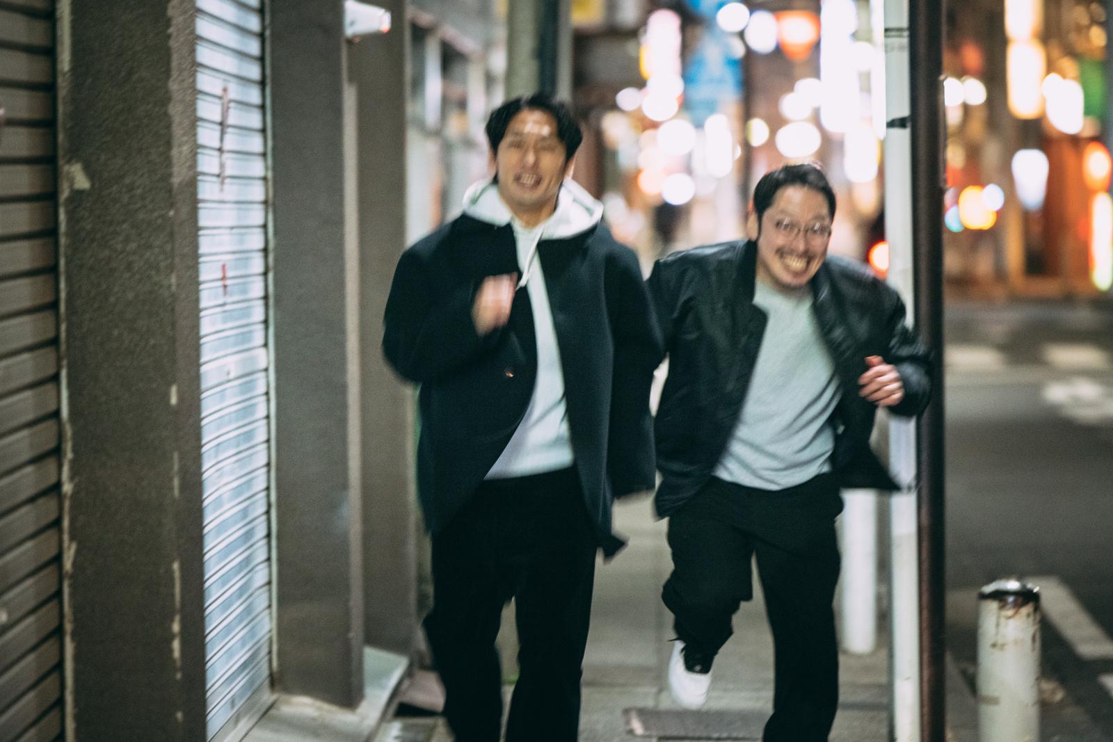 Two male detectives rushing through the night city streets with their arms around each other