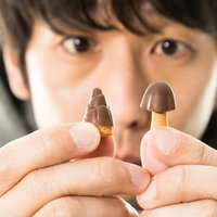 きのこの山とたけのこの里を手に持って見つめる男性の写真