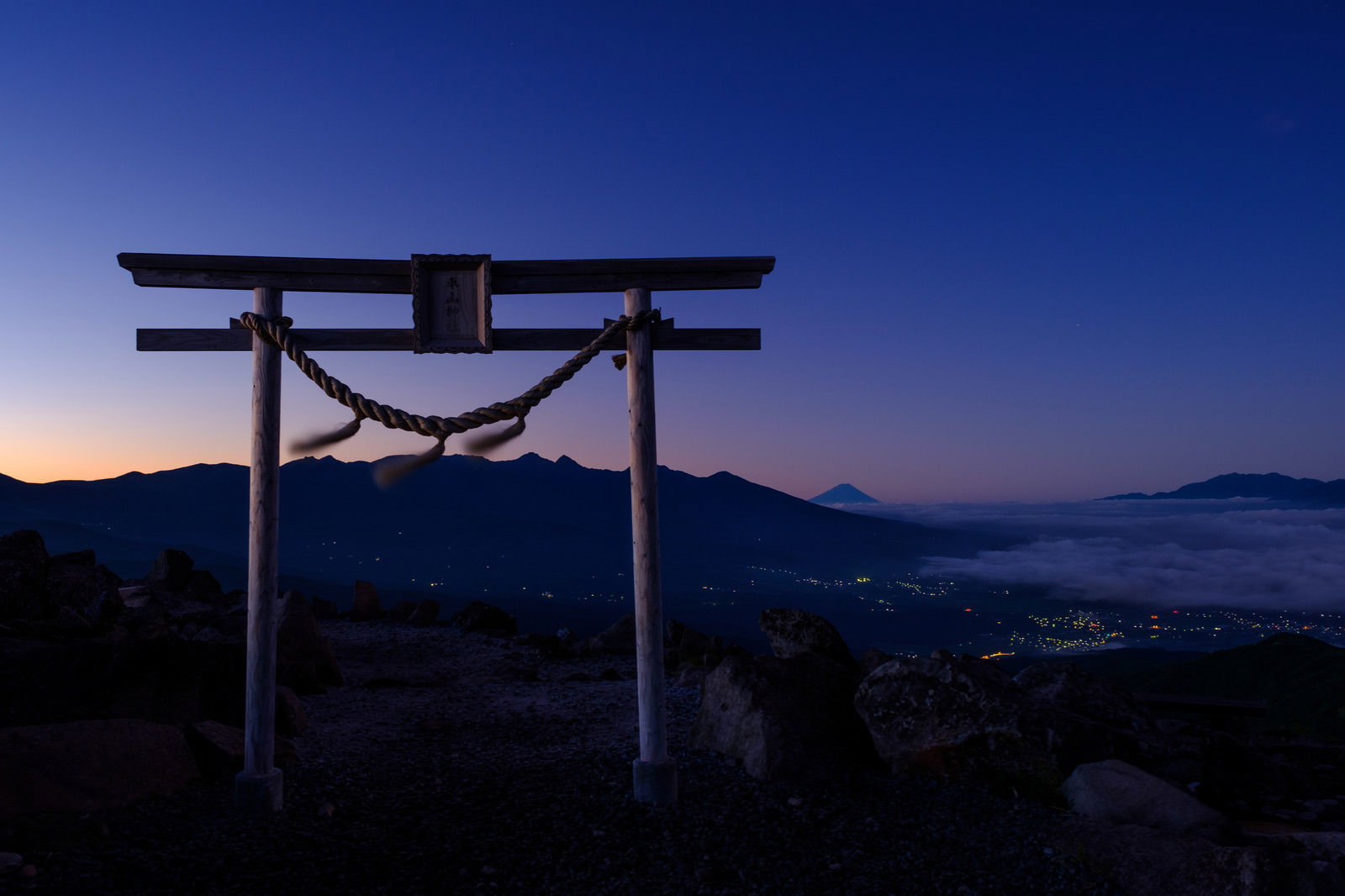 夕暮れ時の霧ヶ峰高原に立つ鳥居のシルエットと遠くの山並み