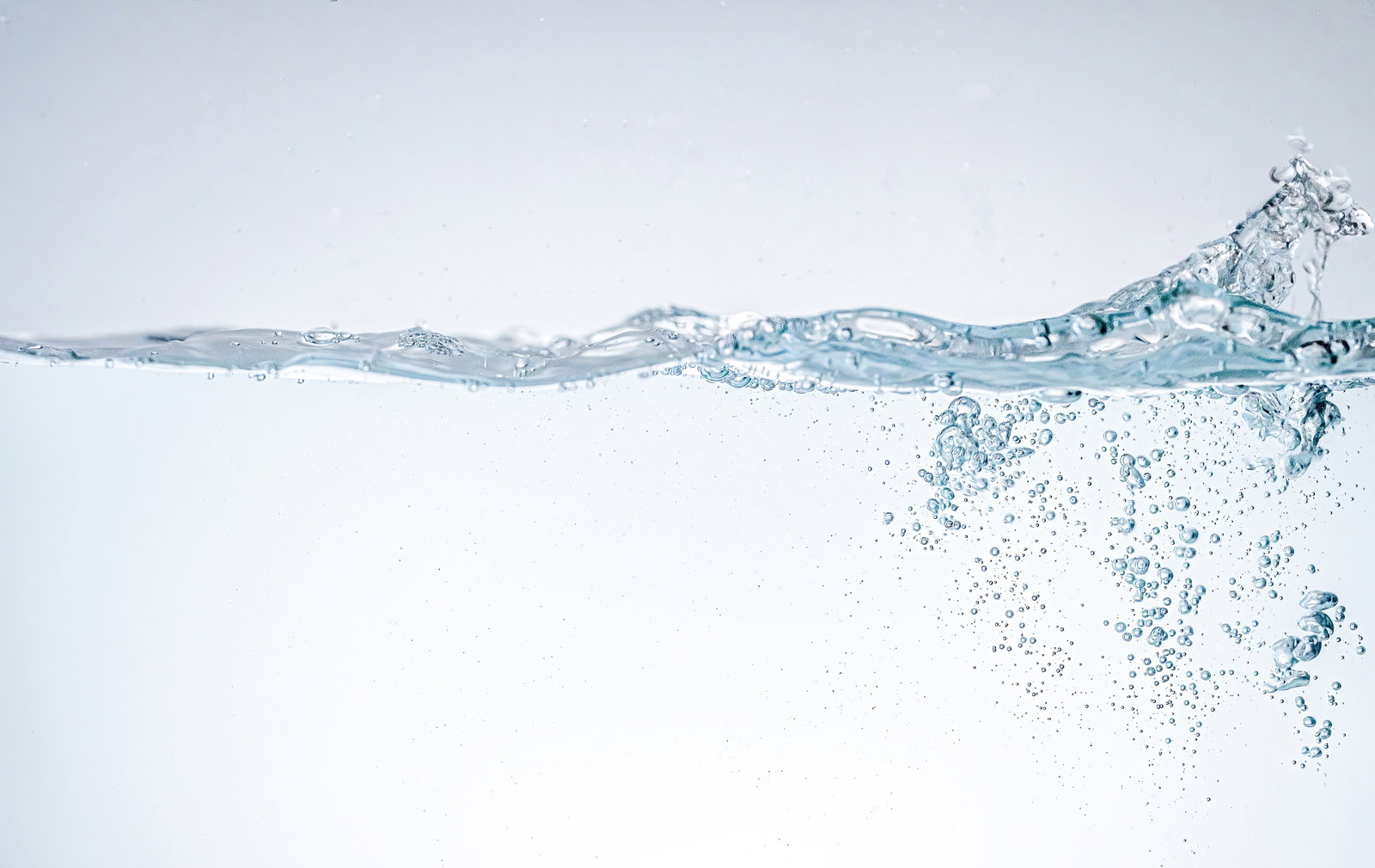 透明な水槽の中で多数の気泡が上昇し、水面で波紋と共に集合している