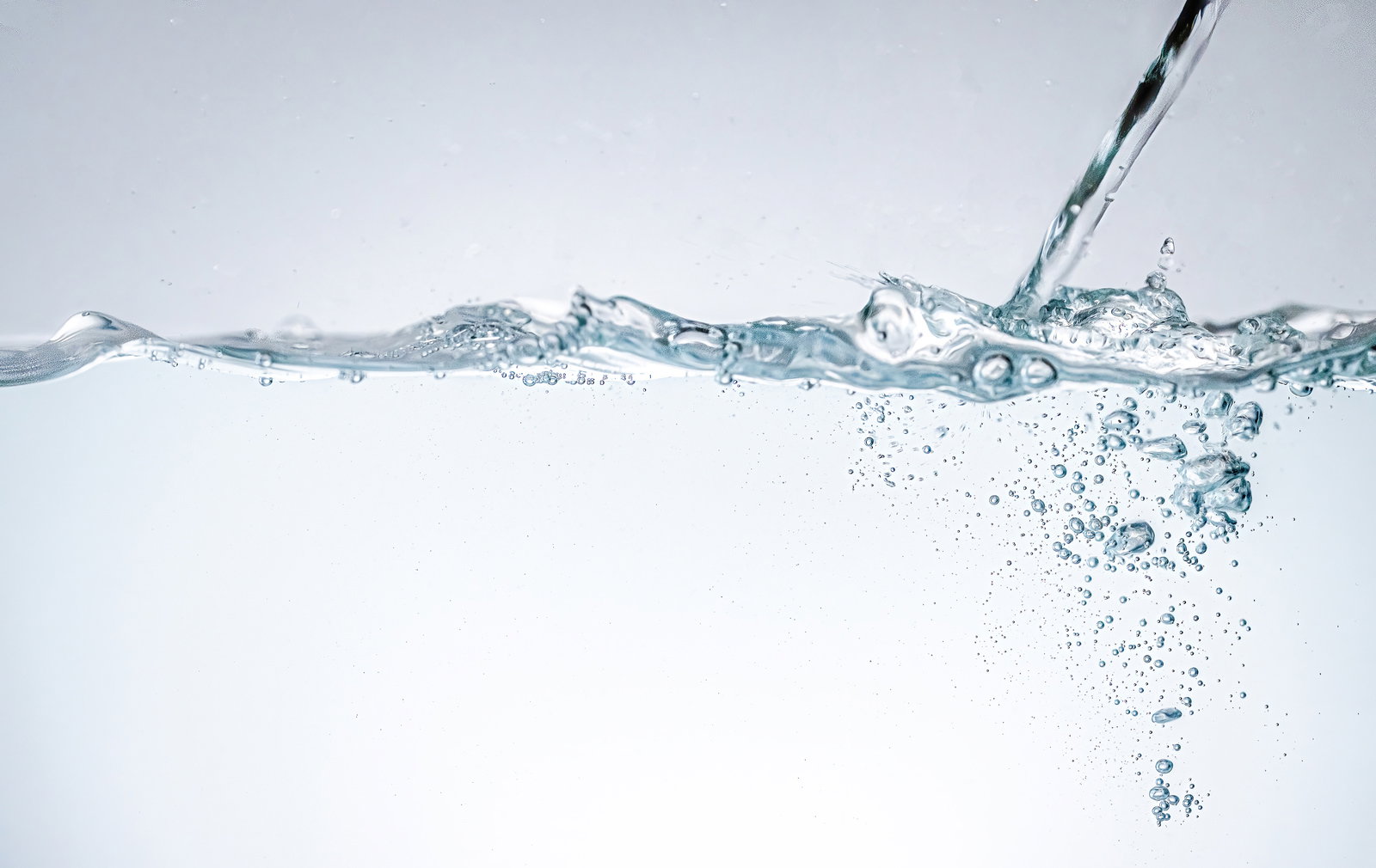 透明な水に気泡が浮かぶ注水の写真。水面の波紋と液体の流れ