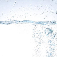 透明な水面に落ちる水滴と立ち上がる気泡の写真