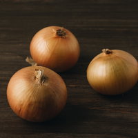 木のテーブルに無造作に置かれた3個の玉葱の写真