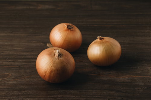 木製机に置かれた3個の玉葱と影の食材