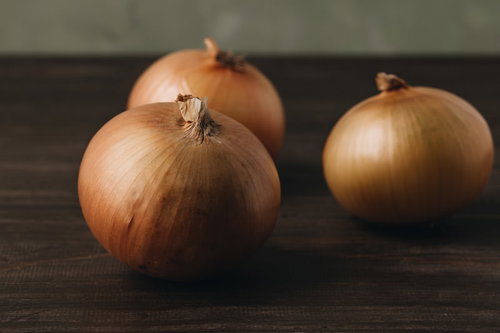 木製テーブルに並べた三個の玉葱、茶色い皮