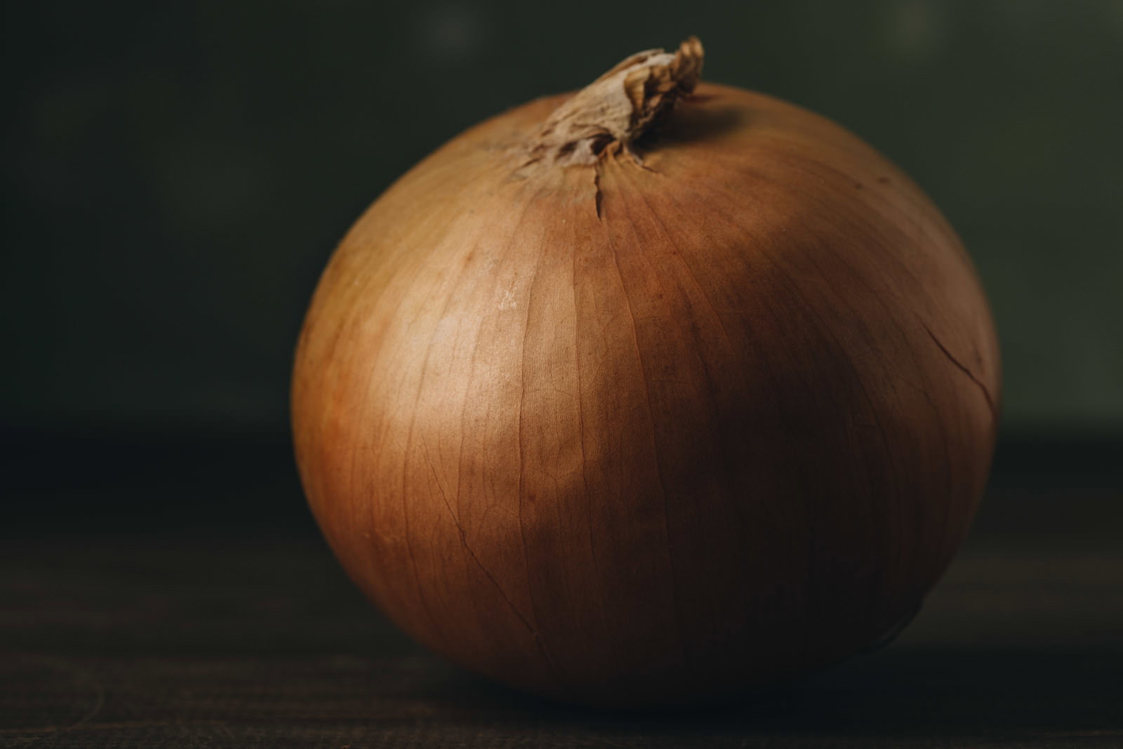 茶色い薄皮に包まれた丸いタマネギ1個が暗い背景に置かれている