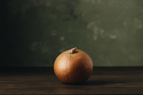木製テーブルに置かれた玉葱の表面に残る光と影